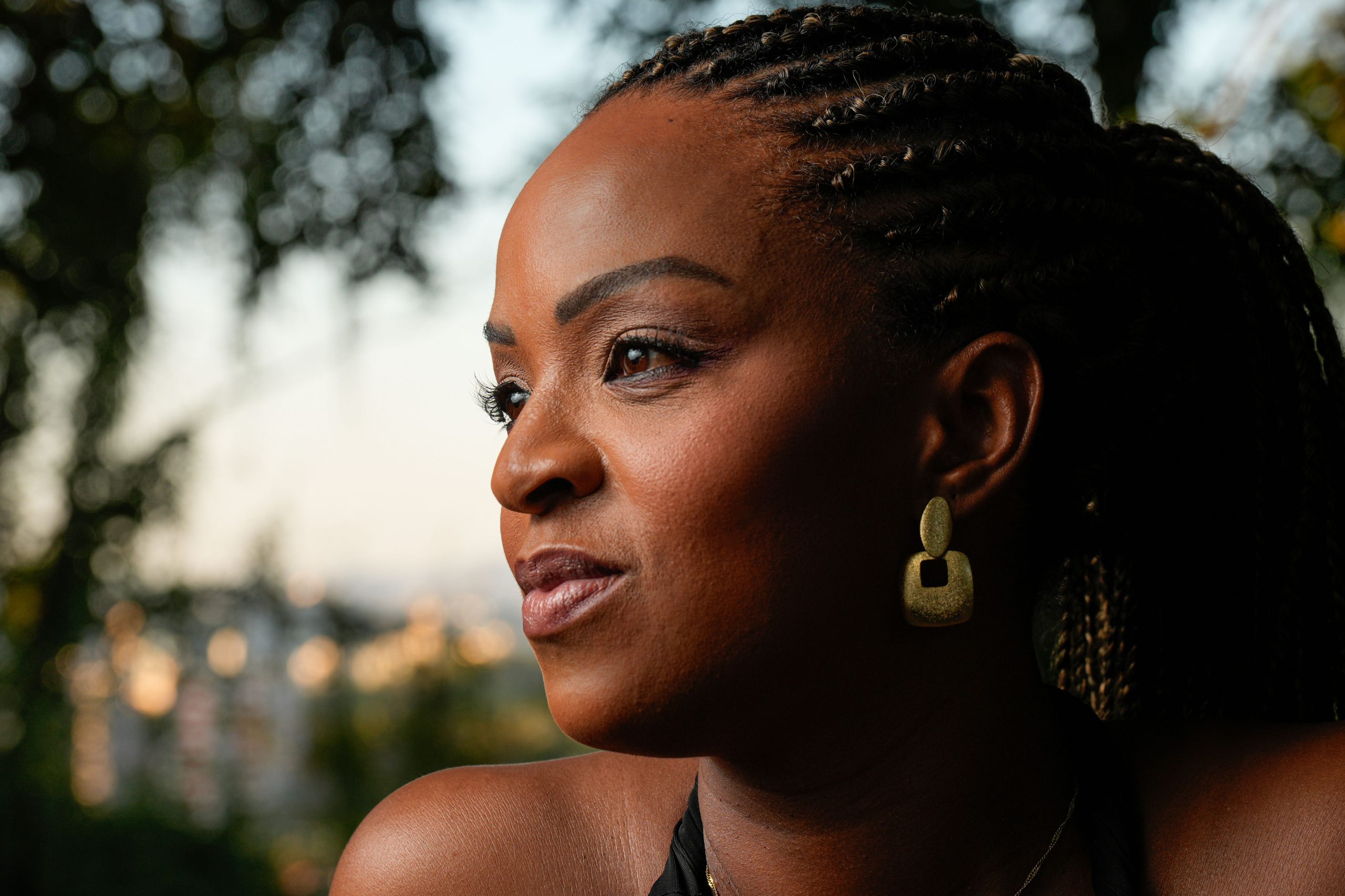 Close-up portrait of a woman with braided hair and earrings in a natural outdoor setting.